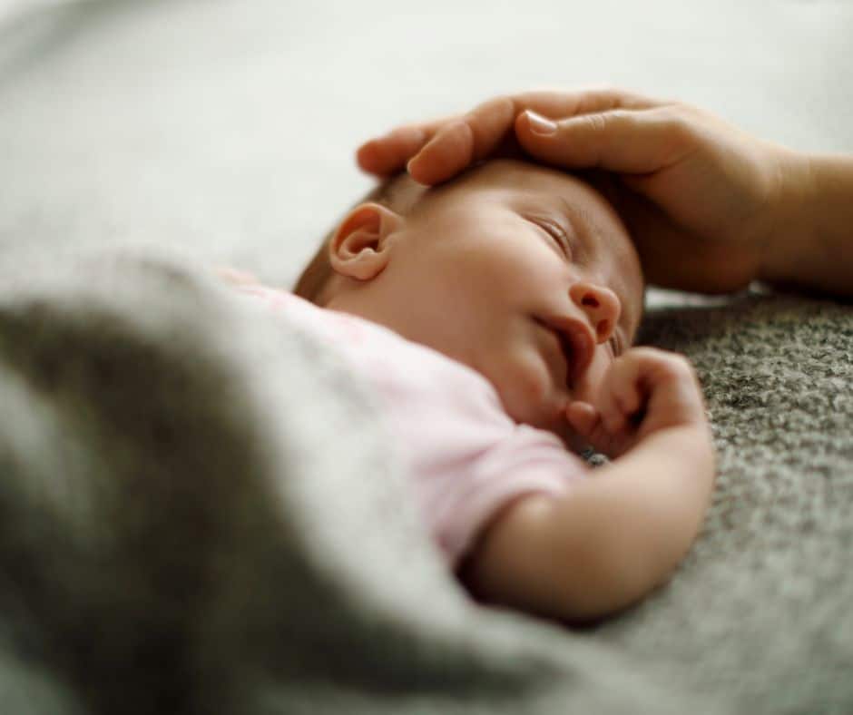 Newborn with mom's hand gently and lovingly placed on her newborns head.